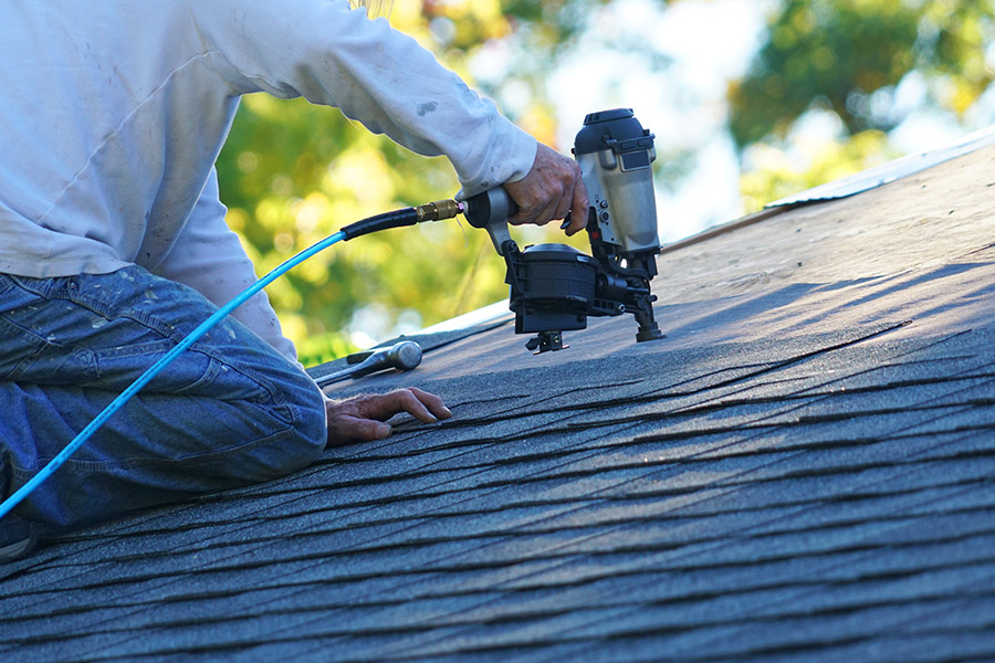 contractor close up on top of roof with nailgun installing asphalt shingles claremore ok